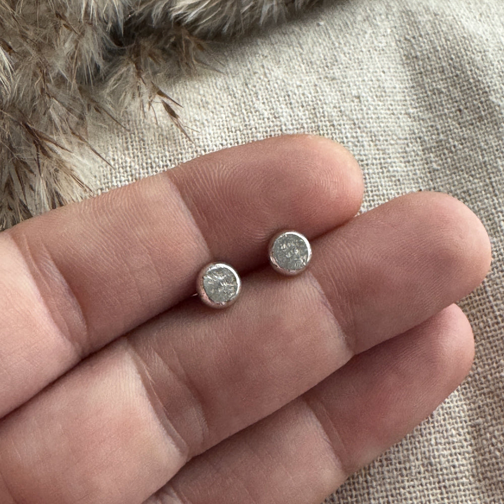 Two stud earrings held between fingers against a textured fabric background
