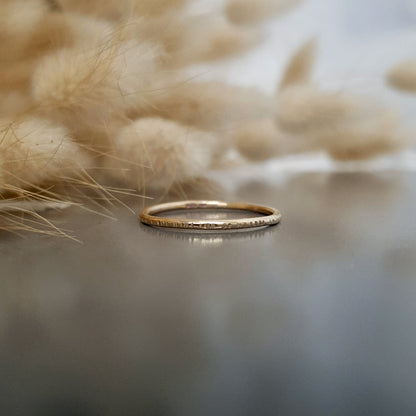 A 9ct gold hammered lines stacking ring placed on a textured surface, with a soft focus background.