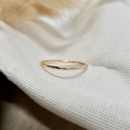 A single hammered gold stacking ring displayed against a neutral background with dried flowers to the side.