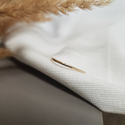 A single hammered gold stacking ring displayed against a neutral background with dried flowers to the side.