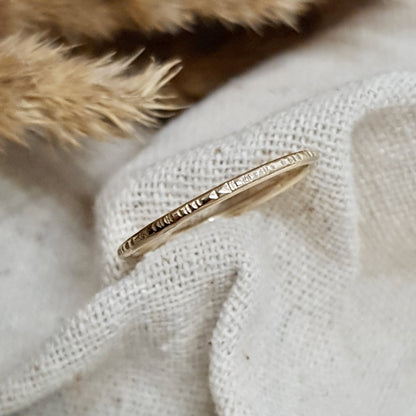 A 9ct gold hammered lines stacking ring placed on a  cream textured  fabric 