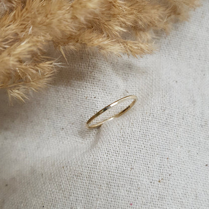 A flat textured 9ct gold stacking ring on a linen surface, with a hammered finish and a shadow falling on the linen from a feather object behind it.