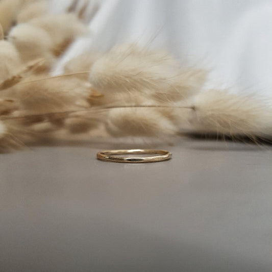 A 9ct gold hexagonal stacking ring on a textured surface, with dried fluffy plants behind it