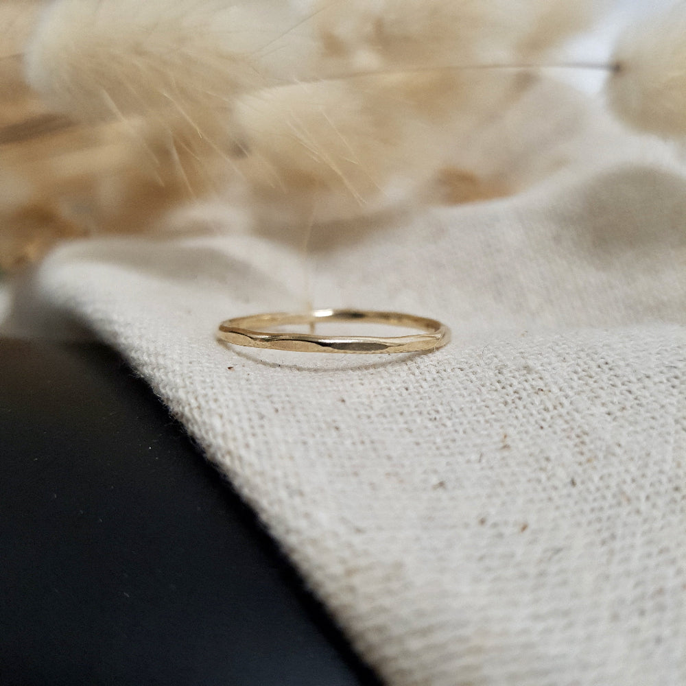 A 9ct gold hexagonal stacking ring on a cream textured surface, with dried fluffy plants behind it