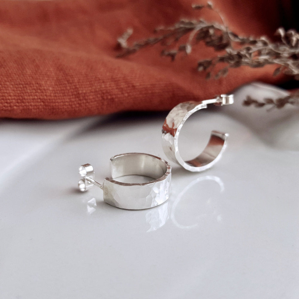 Chunky 6mm wide Silver Hoops Earrings with a hammered finish on a white surface with orange fabric in the background