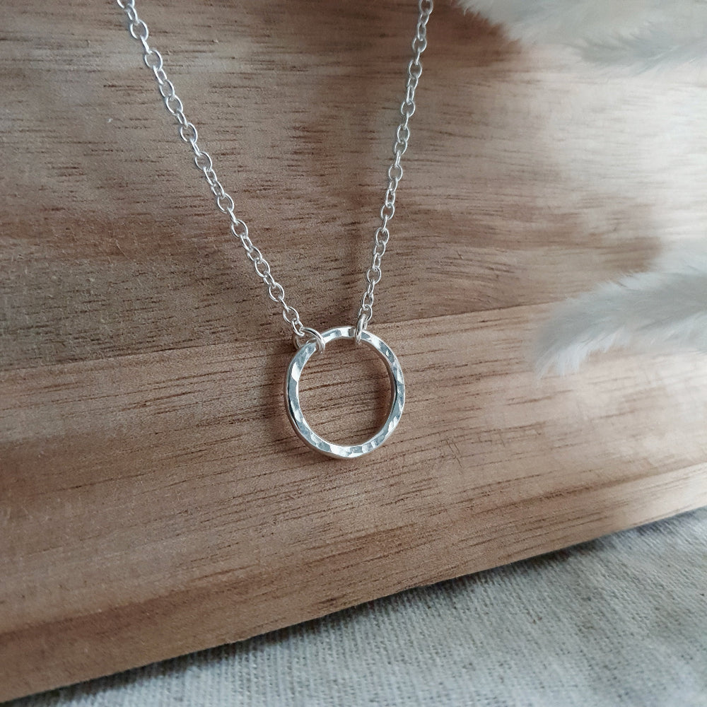 Silver circle pendant on chain displayed on a wooden background