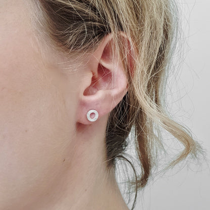A close up of a ladies ear with a small silver circle stud earring