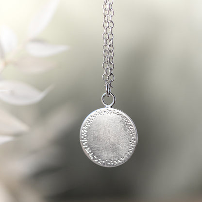 a silver pendant with a textured edge hanging on a delicate chain on a blurred background