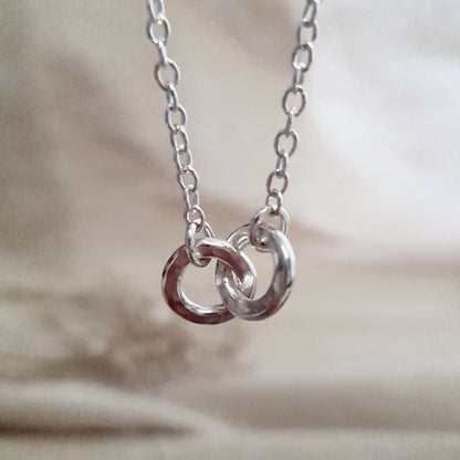 2 hammered silver links interlocked on a silver chain with a cream blurred background