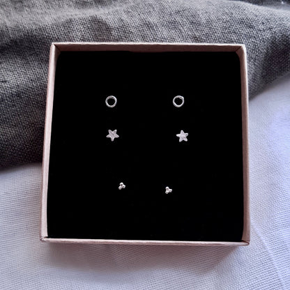 Set of 3 pairs of small silver stud earrings presented in a gift box with a black insert. Set 1 are circles, set 2 are stars and Set 3 is 3 small balls forming a triangle