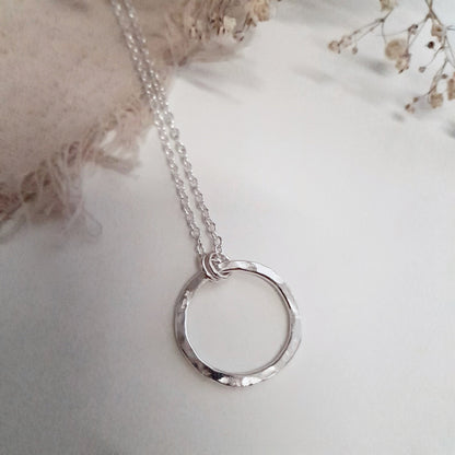 A silver eternity necklace with a hammered circle pendant and two little links connecting it to the chain, on a white background