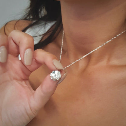 silver flower necklace being worn by a lady with long dark hair ad she is holding the pendant
