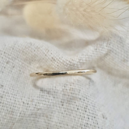 A flat textured 9ct gold stacking ring on a linen surface, with a hammered finish and  on white linen with a feather behind it.