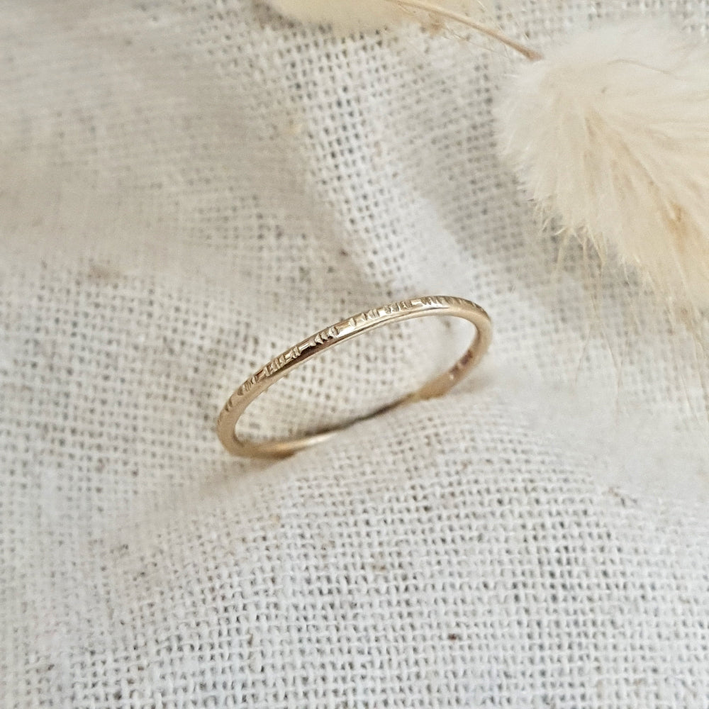 A 9ct gold hammered lines stacking ring placed on a textured surface, with a soft focus background.