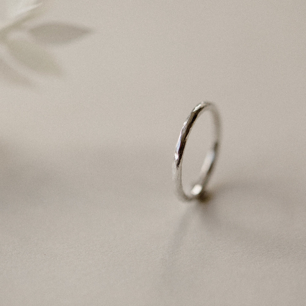 A silver infinity ring with a hammered finish, placed on a beige background.