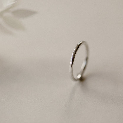A silver infinity ring with a hammered finish, placed on a beige background.