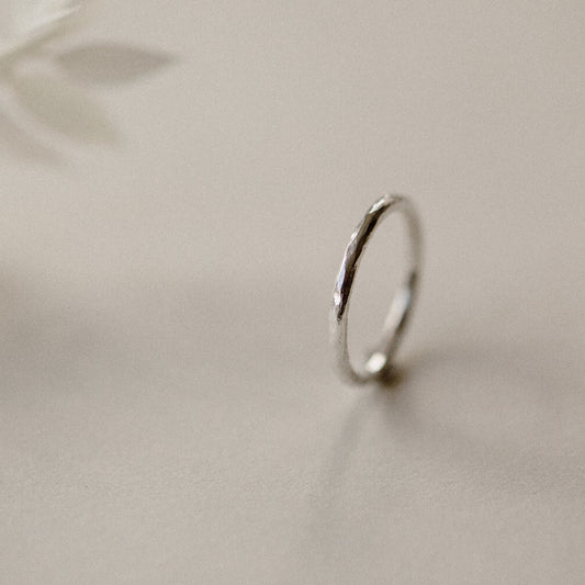 A silver infinity ring with a hammered finish, placed on a beige background.