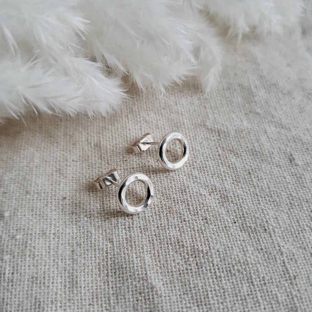 A pair of sterling silver hammered circle stud earrings resting on a white fabric surface.