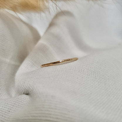 A single hammered gold stacking ring displayed against a neutral background with dried flowers to the side.