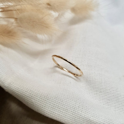 A single hammered gold stacking ring displayed against a neutral background with dried flowers to the side.