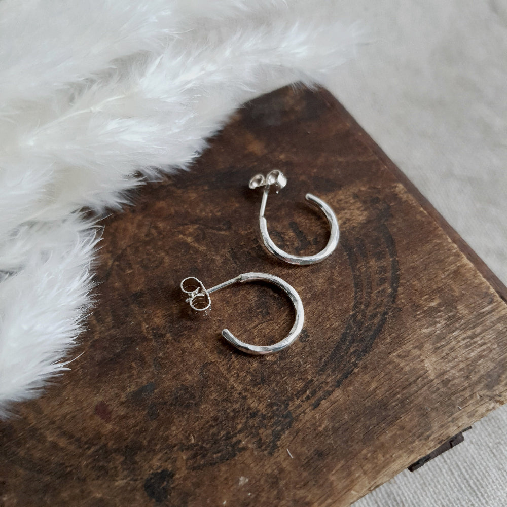 A pair of silver hammered hoop earrings resting on a wooden surface with a furry object in the background.