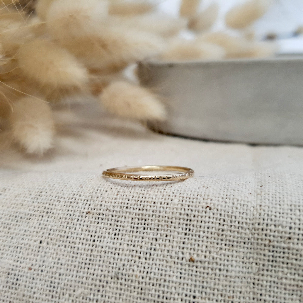A 9ct gold hammered lines stacking ring placed on a textured surface, with a soft focus background.