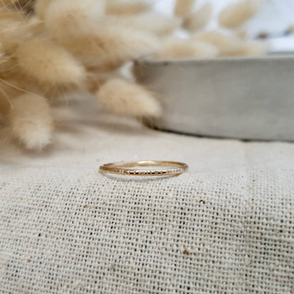A 9ct gold hammered lines stacking ring placed on a textured surface, with a soft focus background.