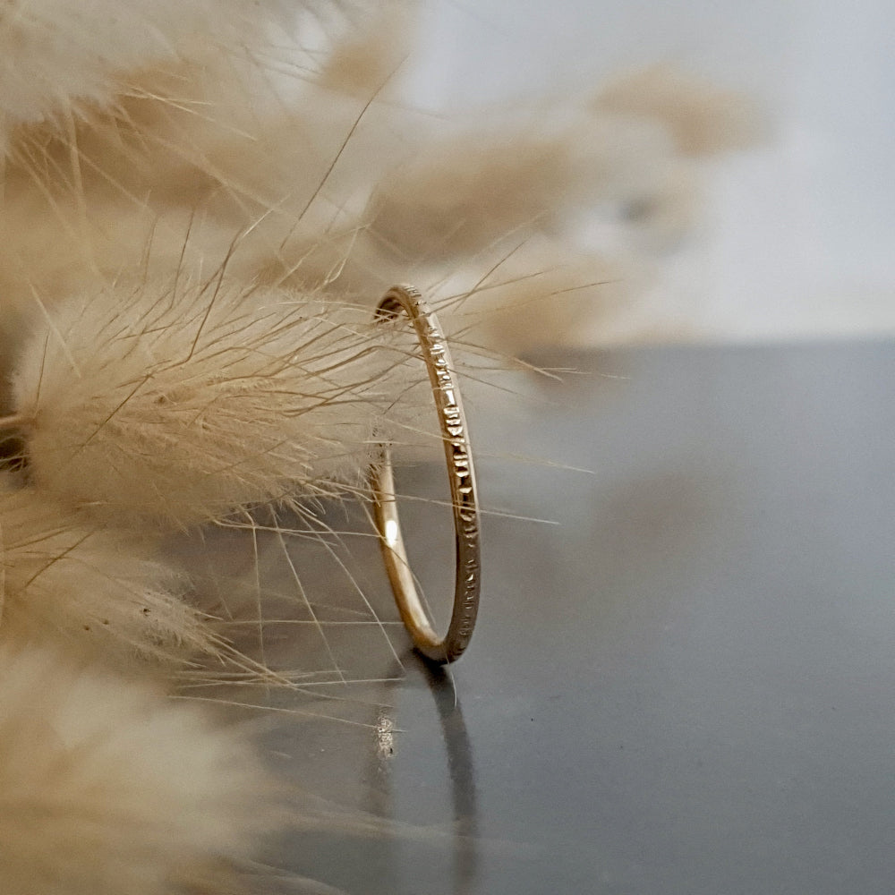 A 9ct gold hammered lines stacking ring placed on a textured surface, with a soft focus background.