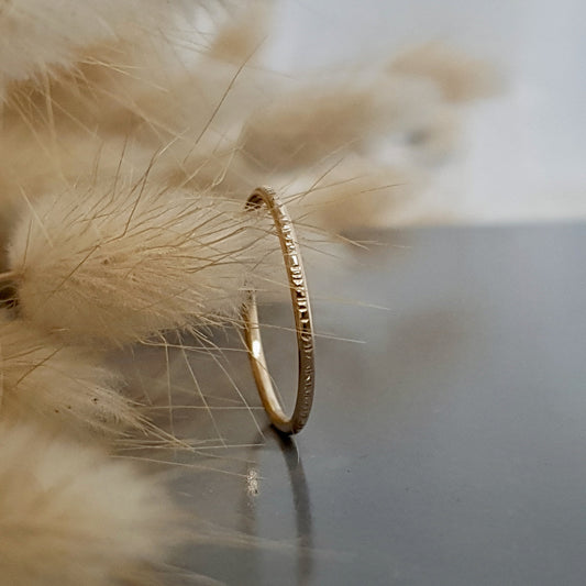 A 9ct gold hammered lines stacking ring placed on a textured surface, with a soft focus background.
