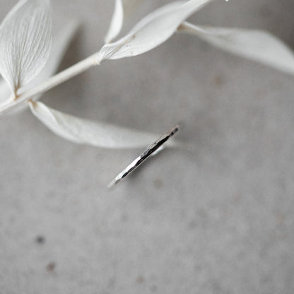 A single hammered silver stacking ring placed on a grey surface, with delicate white leaves