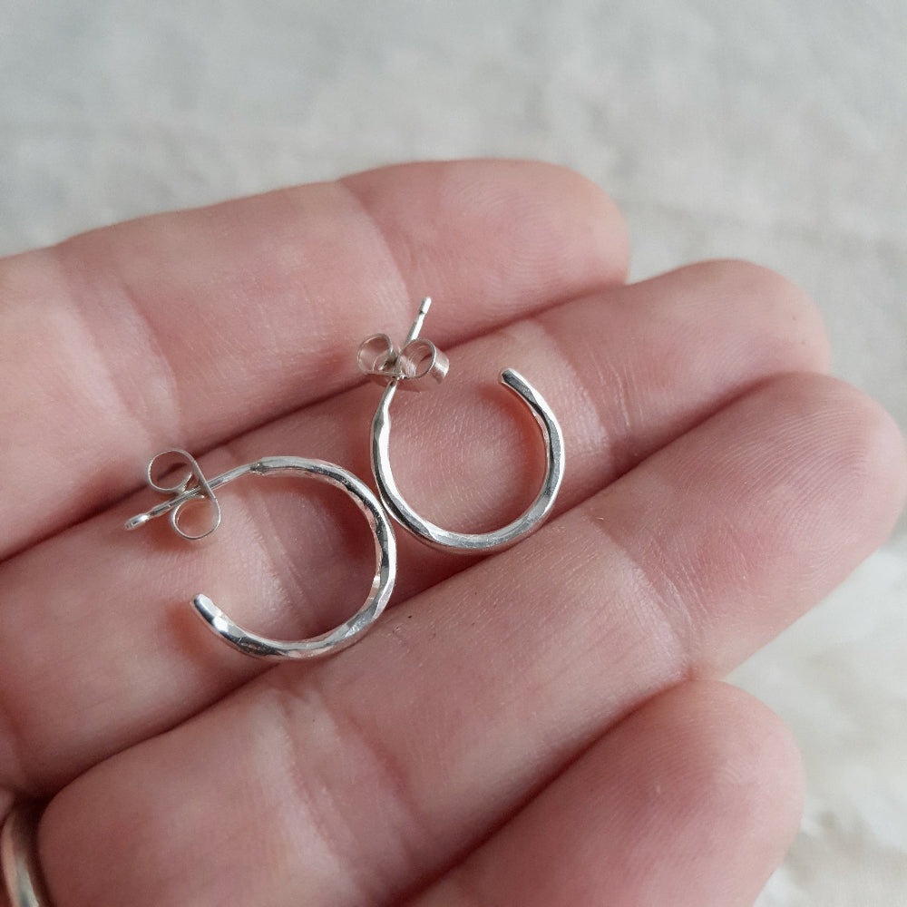 A pair of silver hammered open hoop earrings reing held on an open hand.