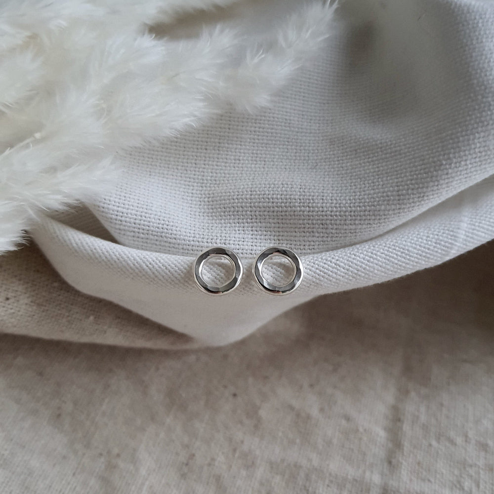A pair of sterling silver hammered circle stud earrings resting on a white fabric surface.