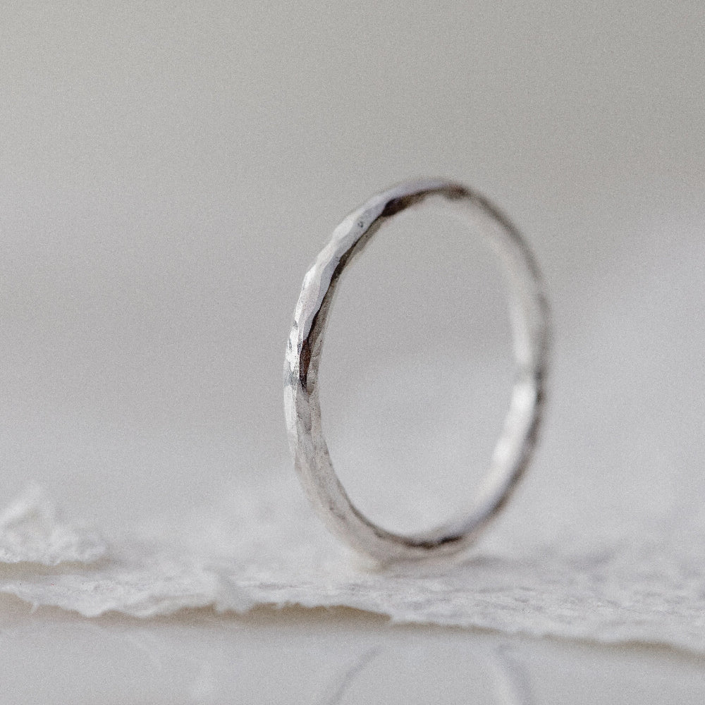 A Silver hammered round 2mm ring on a white textured paper background