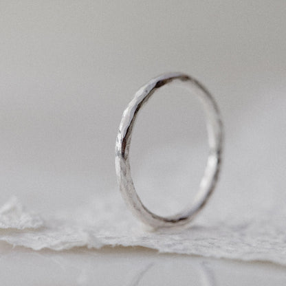 A Silver hammered round 2mm ring on a white textured paper background
