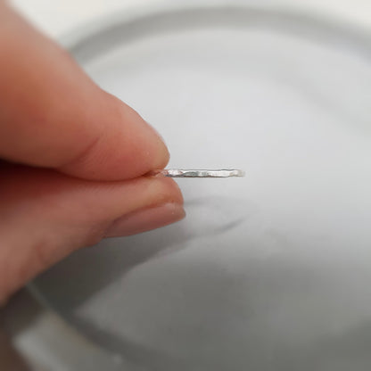 A single hammered silver stacking ring being held between the first finger and the thumb