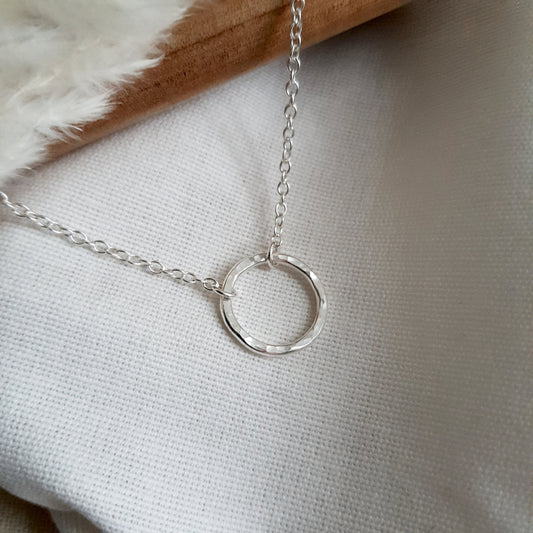 Silver hammered circle pendant with chain  to form a necklace on a cream fabric background