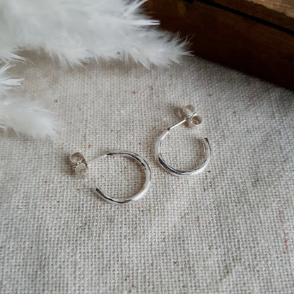 A pair of silver hammered hoop earrings resting on a cream textured fabric with a furry object in the background.