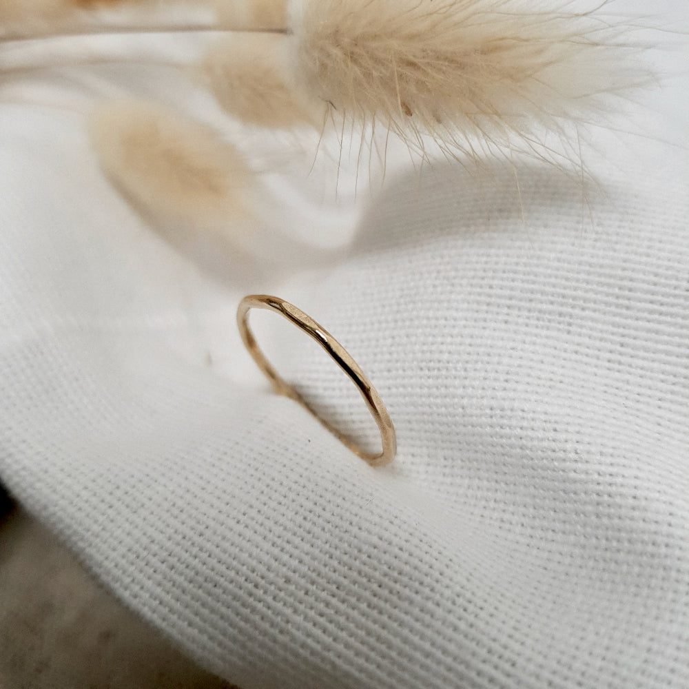 A 9ct gold hexagonal stacking ring on a cream textured fabric, with dried fluffy plants behind it