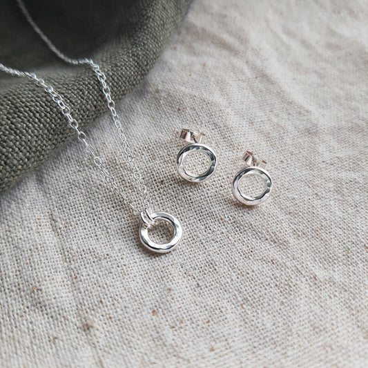 A silver circle link pendant with a hammered finish and a pair of matching stud earrings on a cream fabric background