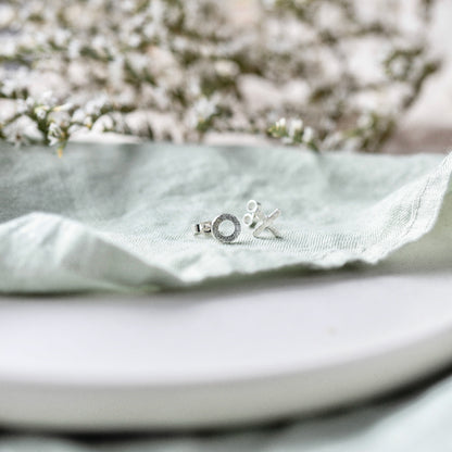 Hugs and Kisses silver stud earrings on a pale mint green fabric with foliage in the background