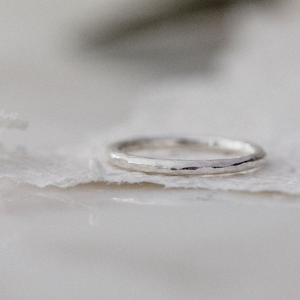 a silver hammered ring laying down on a white background of textured paper
