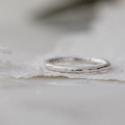 a silver hammered ring laying down on a white background of textured paper