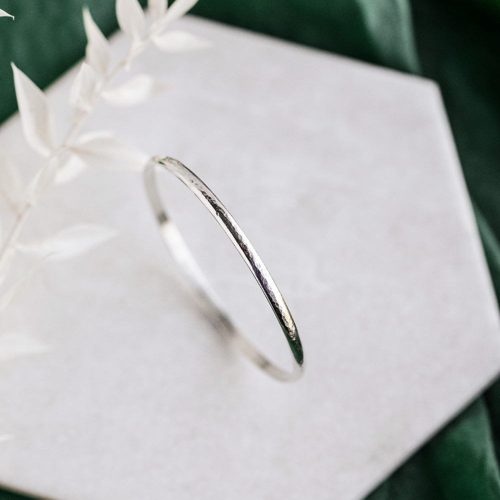 A silver bangle bracelet with a hammered texture, displayed on a white surface.