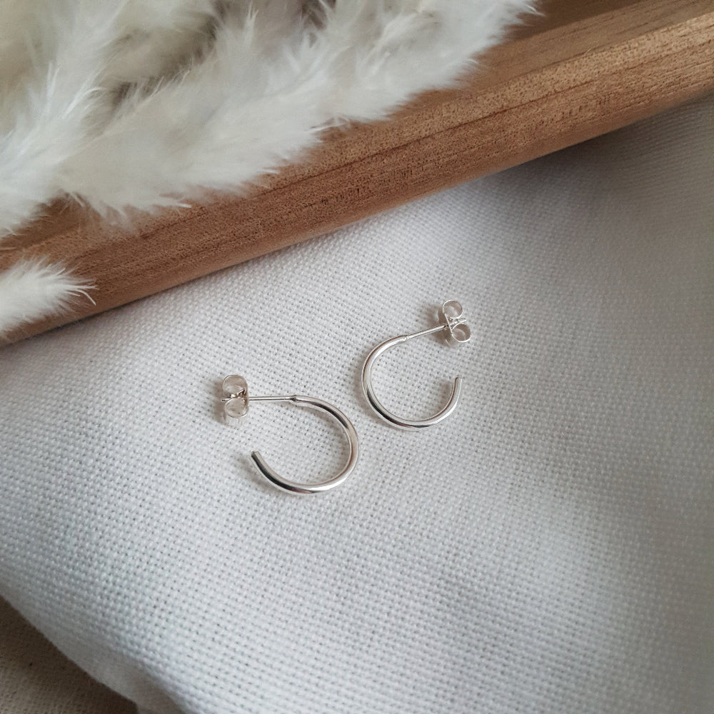A pair of silver hoop earrings placed on a white fabric surface.
