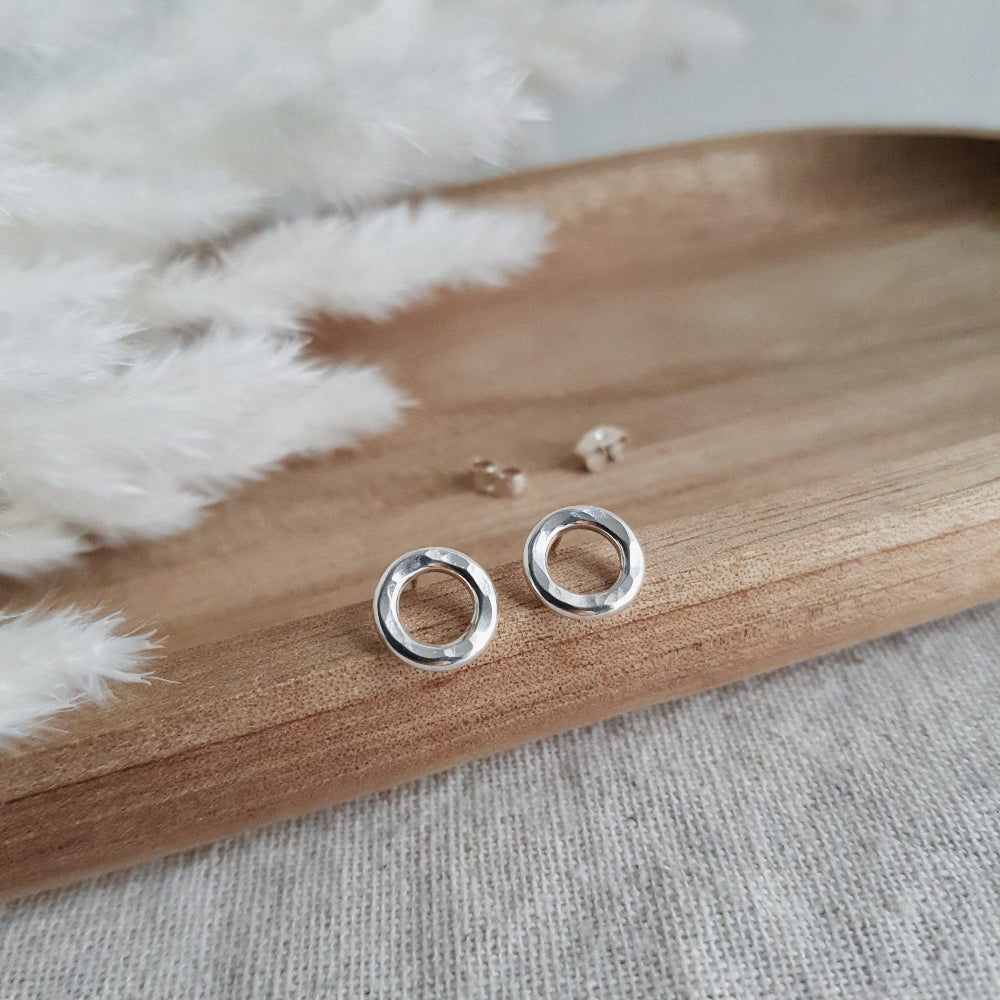 A pair of sterling silver hammered circle stud earrings resting on a wooden tray