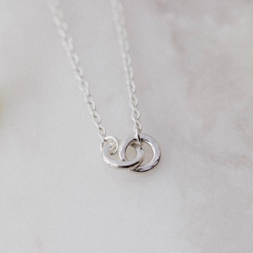 2 hammered silver links interlocked on a silver chain with a cream blurred background