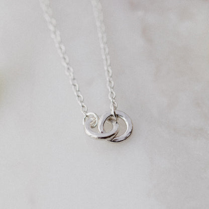 2 hammered silver links interlocked on a silver chain with a cream blurred background