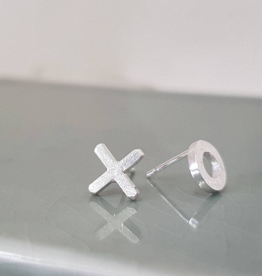 A pair of mismatched silver stud earrings one is a circle the other an X on a pale green background