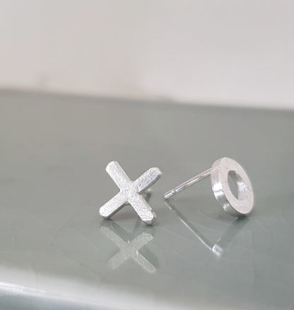 A pair of mismatched silver stud earrings one is a circle the other an X on a pale green background
