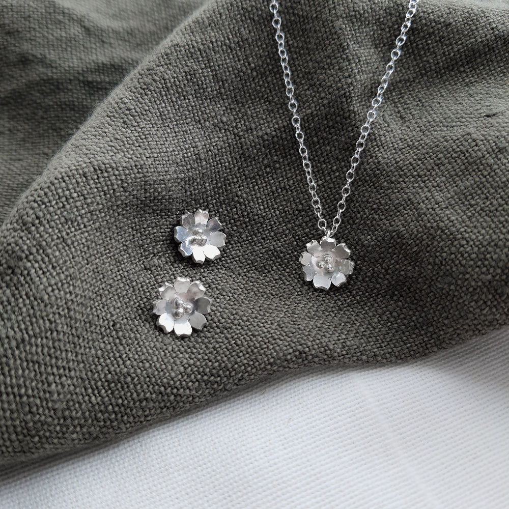 silver flower earrings and necklace on a green fabric background